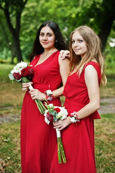 Duas damas de honra de meninas em vestidos vermelhos com buquês de casamento . — Fotografia de Stock