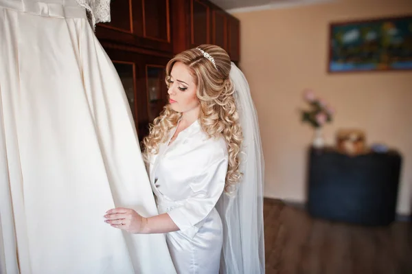 Beautiful blonde curly bride at silk robe looking at her wedding — Stock Photo, Image