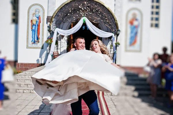 Novio sosteniendo novia en las manos después de la ceremonia de boda en la iglesia . — Foto de Stock