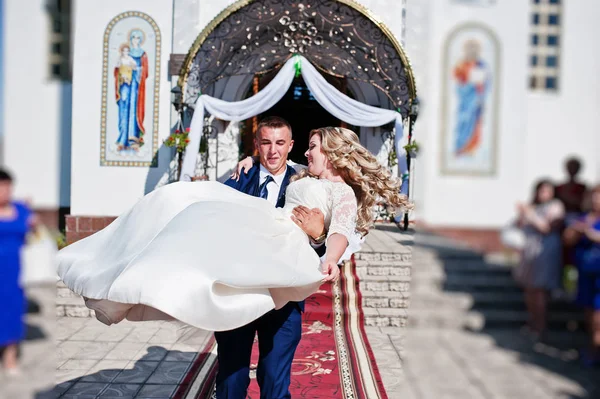 Novio sosteniendo novia en las manos después de la ceremonia de boda en la iglesia . — Foto de Stock