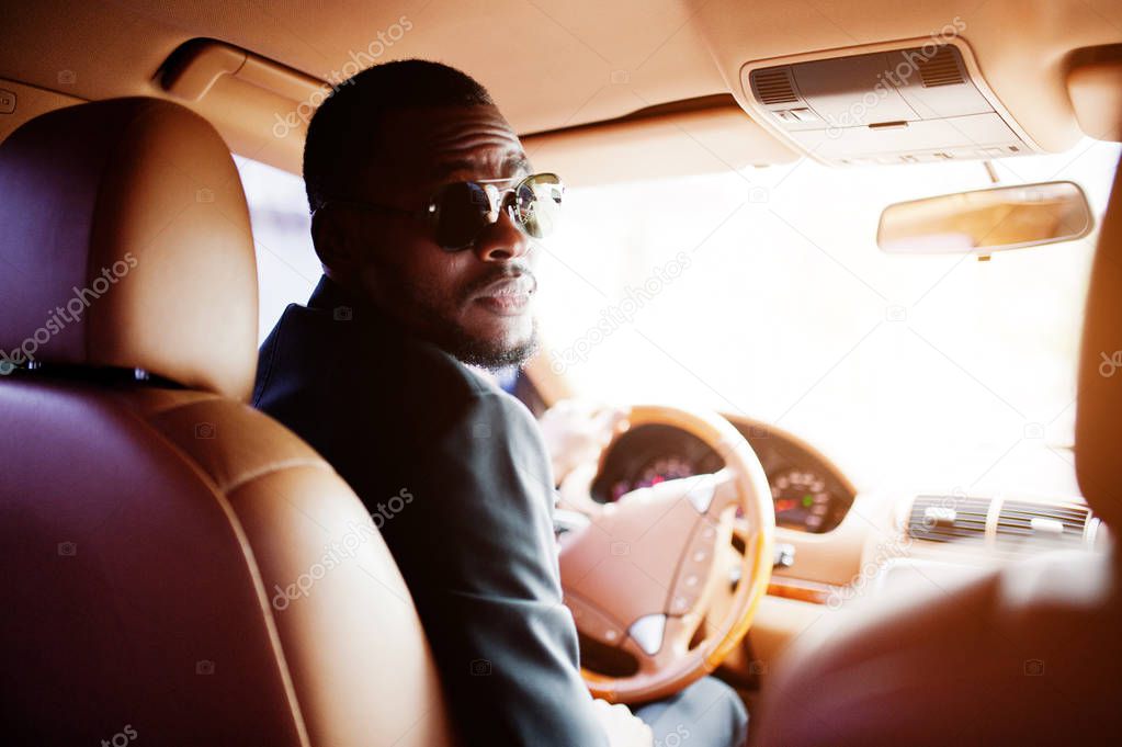 Stylish black man sitting behind the wheel of luxury car. Rich a
