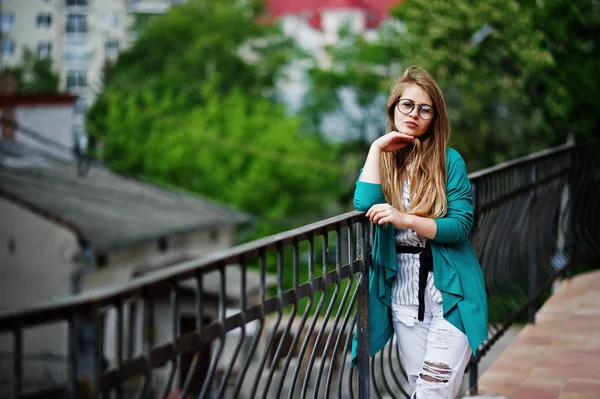 Chica de moda en gafas y pantalones vaqueros rasgados contra la barrera en stree — Foto de Stock