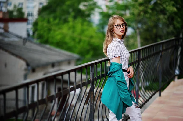Trendy meisje op bril en gescheurde jeans tegen versperring op stree — Stockfoto