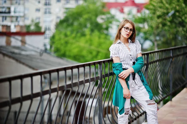 Trendig tjej på glasögon och rippade jeans mot barriär på stree — Stockfoto