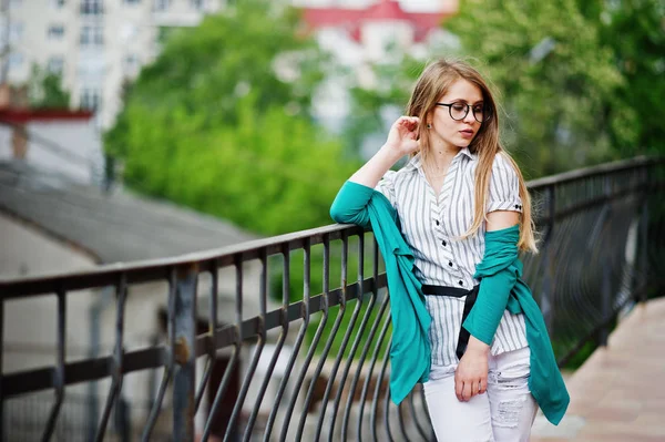 Модная девушка в очках и порванные джинсы против барьера на улице — стоковое фото