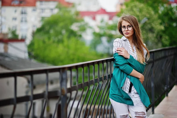 Chica de moda en gafas y pantalones vaqueros rasgados contra la barrera en stree —  Fotos de Stock