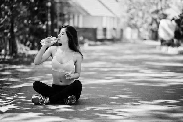 Fitness sport girl in sportswear sitting on road at street and d