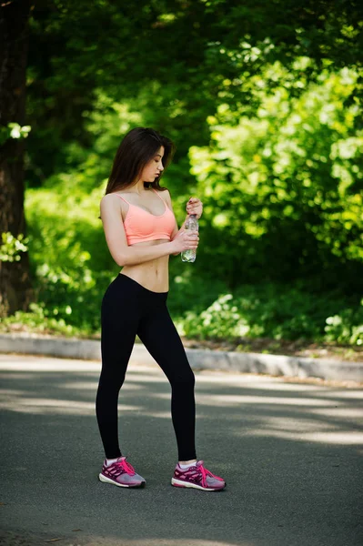 Фітнес-спортивна дівчина в спортивному одязі, позують на дорозі в парку з пляшкою — стокове фото
