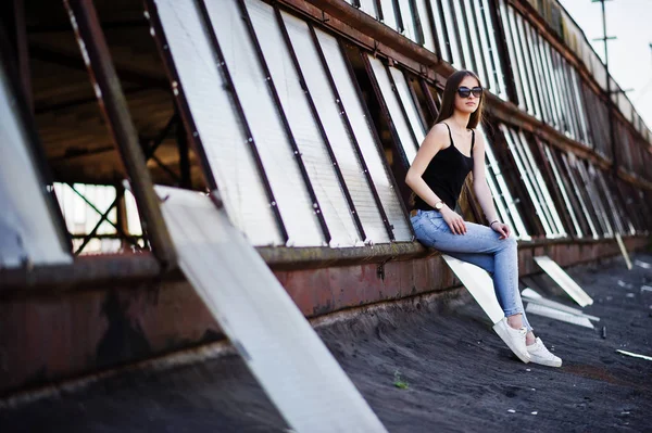 Ragazza a occhiali da sole e jeans posato sul tetto di indus abadoned — Foto Stock