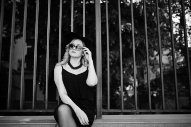 Siyah elbise, güneş gözlüğü, kolyeler ve şapkasını tekrar sarışın kadın