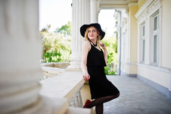 Mujer rubia en vestido negro, collares y sombrero contra vintage h — Foto de Stock