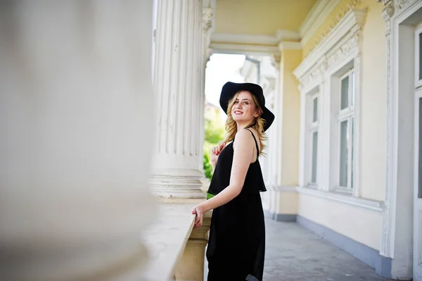 Blond žena v černých šatech, náhrdelníky a klobouk proti vintage h — Stock fotografie