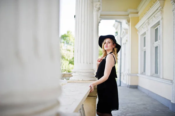 Blond žena v černých šatech, náhrdelníky a klobouk proti vintage h — Stock fotografie