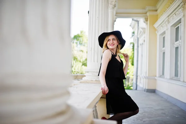 Mujer rubia en vestido negro, collares y sombrero contra vintage h —  Fotos de Stock