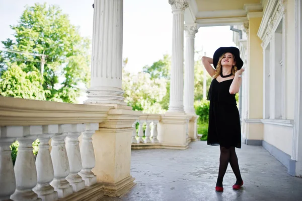 Mulher loira em vestido preto, colares e chapéu contra o vintage h — Fotografia de Stock