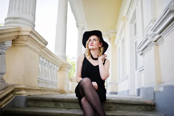 Mujer rubia en vestido negro, collares y sombrero contra vintage h — Foto de Stock