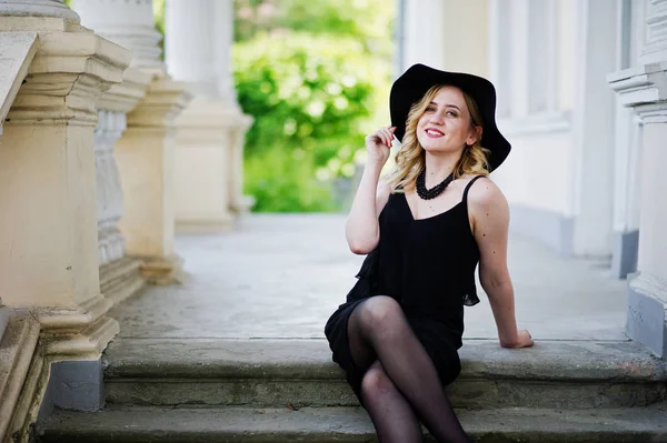 Mujer rubia en vestido negro, collares y sombrero contra vintage h — Foto de Stock