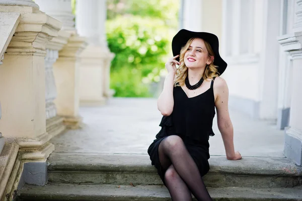 Blond kvinna på svart klänning, halsband och hat mot vintage h — Stockfoto