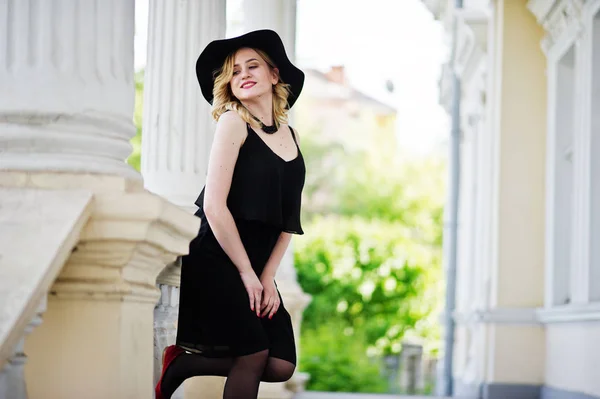 Blonde woman on black dress, necklaces and hat against vintage h — Stock Photo, Image