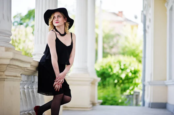 Mujer rubia en vestido negro, collares y sombrero contra vintage h —  Fotos de Stock