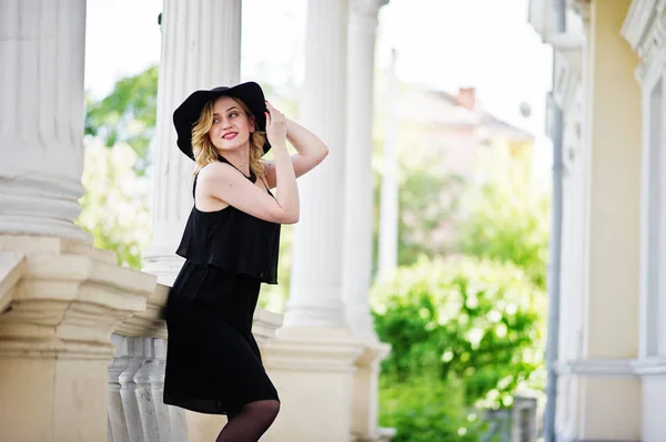 Blonde woman on black dress, necklaces and hat against vintage h — Stock Photo, Image