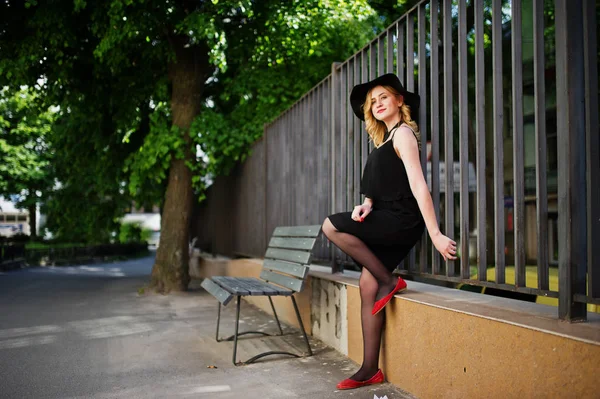 Femme blonde sur robe noire, colliers et chapeau reprend clôture en fer — Photo