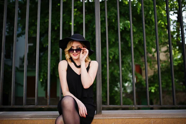 Femme blonde sur robe noire, lunettes de soleil, colliers et chapeau à nouveau — Photo