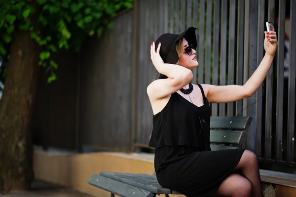 Mulher loira em vestido preto, óculos de sol, colares e chapéu sitti — Fotografia de Stock