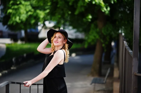 Blondynka na czarnej sukni, naszyjniki i kapelusz stwarzane na ulicach. — Zdjęcie stockowe