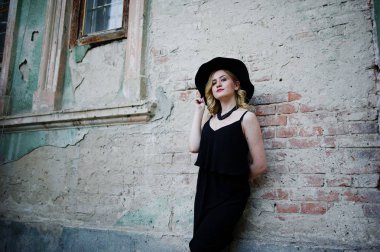 Siyah elbise, kolyeler ve şapkasını eski duvara sarışın kadın 