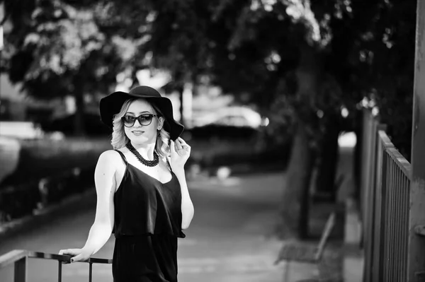 Femme blonde sur robe noire, lunettes de soleil, colliers et chapeau posé — Photo