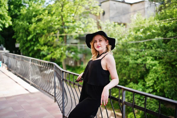 Mulher loira em vestido preto, colares e chapéu agains grades . — Fotografia de Stock