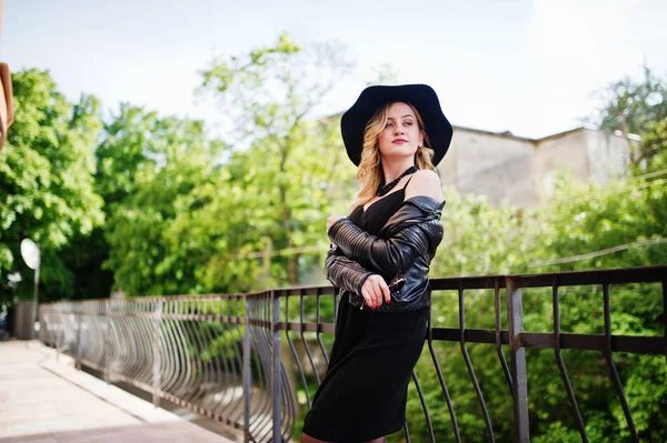 Donna bionda su abito nero, giacca di pelle, collane e cappello a — Foto Stock