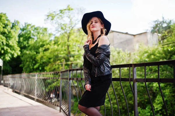 Mujer rubia en vestido negro, chaqueta de cuero, collares y sombrero a —  Fotos de Stock