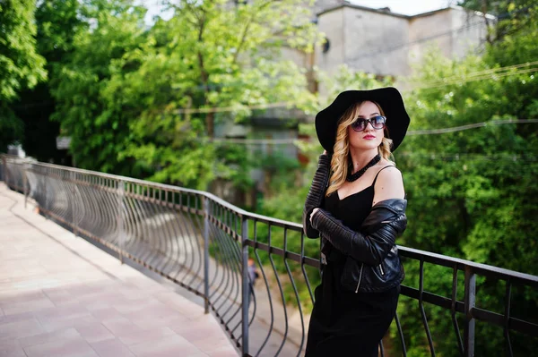 Donna bionda su abito nero, giacca di pelle, occhiali da sole, scollatura — Foto Stock
