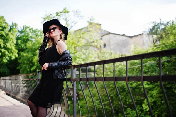 Mujer rubia en vestido negro, chaqueta de cuero, gafas de sol, necklac — Foto de Stock