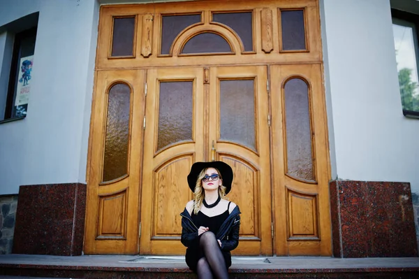 Blond kvinna på svart klänning, skinnjacka, solglasögon, halsband — Stockfoto