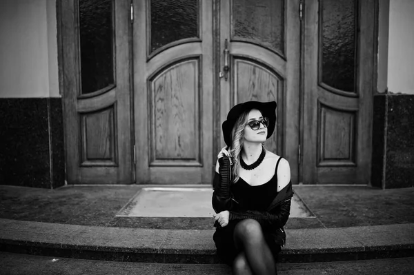 Blond kvinna på svart klänning, skinnjacka, solglasögon, halsband — Stockfoto