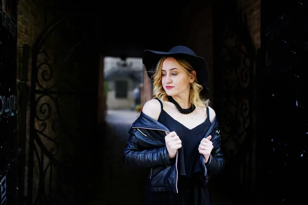Mulher loira em vestido preto, jaqueta de couro, colares e chapéu a — Fotografia de Stock