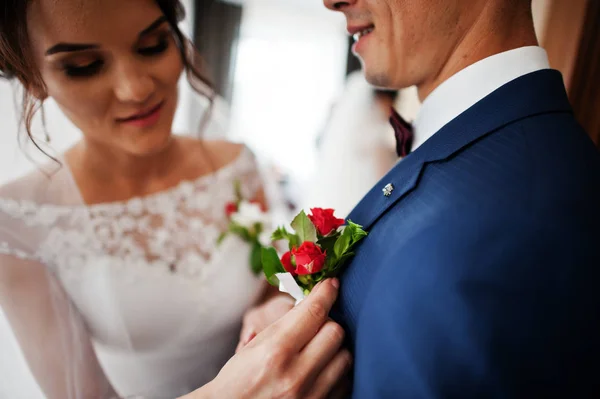 Preciosa novia pone una flor ojal en la chaqueta de un novio . — Foto de Stock