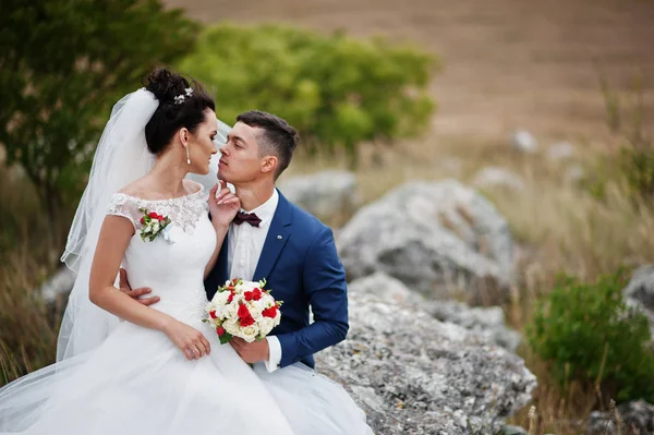 Krásná nevěsta a pohledný ženich sedí na kameni s — Stock fotografie