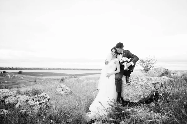 Schöne Braut und schöner Bräutigam sitzen auf dem Stein mit — Stockfoto
