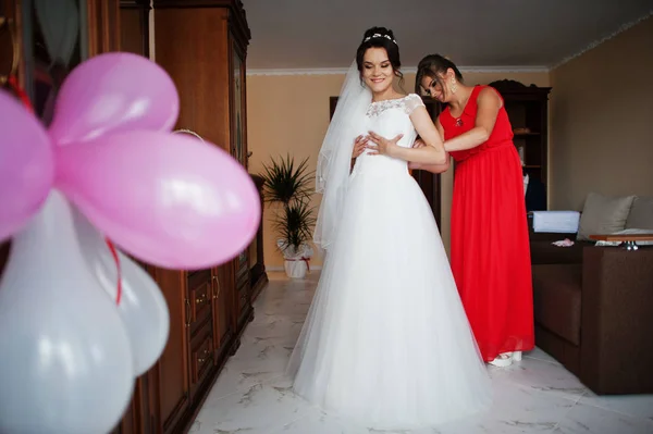 Demoiselle d'honneur aidant à attacher un ruban sur une robe de mariée dans une chambre — Photo