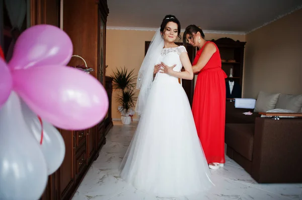 Dama de honra ajudando a atar uma fita em um vestido de casamento em um quarto — Fotografia de Stock