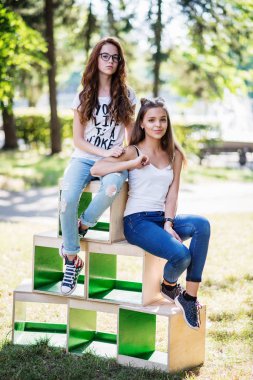 Two gorgeous young girls sitting on wooden boxes in the park on 