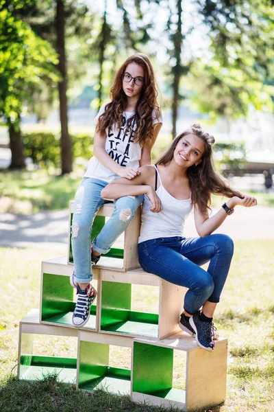 Två vackra unga flickor sitter på trälådor i parken — Stockfoto