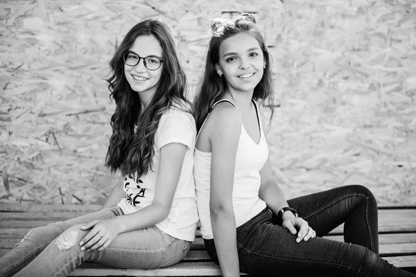 Dos hermosas chicas sentadas en barras de madera contra la pared de chapa. B) — Foto de Stock