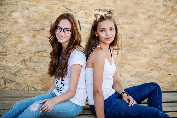 Duas garotas lindas sentadas em barras de madeira contra a parede do folheado . — Fotografia de Stock