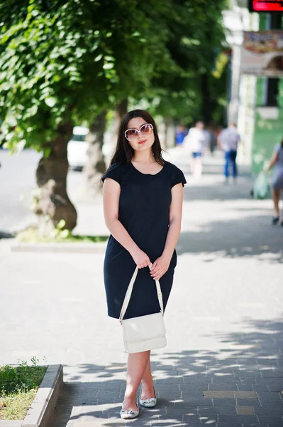 Brunette fille à robe noire sur lunettes de soleil avec sac à main à portée de main — Photo