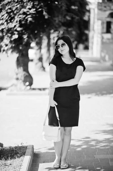 Brunette fille à robe noire sur lunettes de soleil avec sac à main à portée de main — Photo